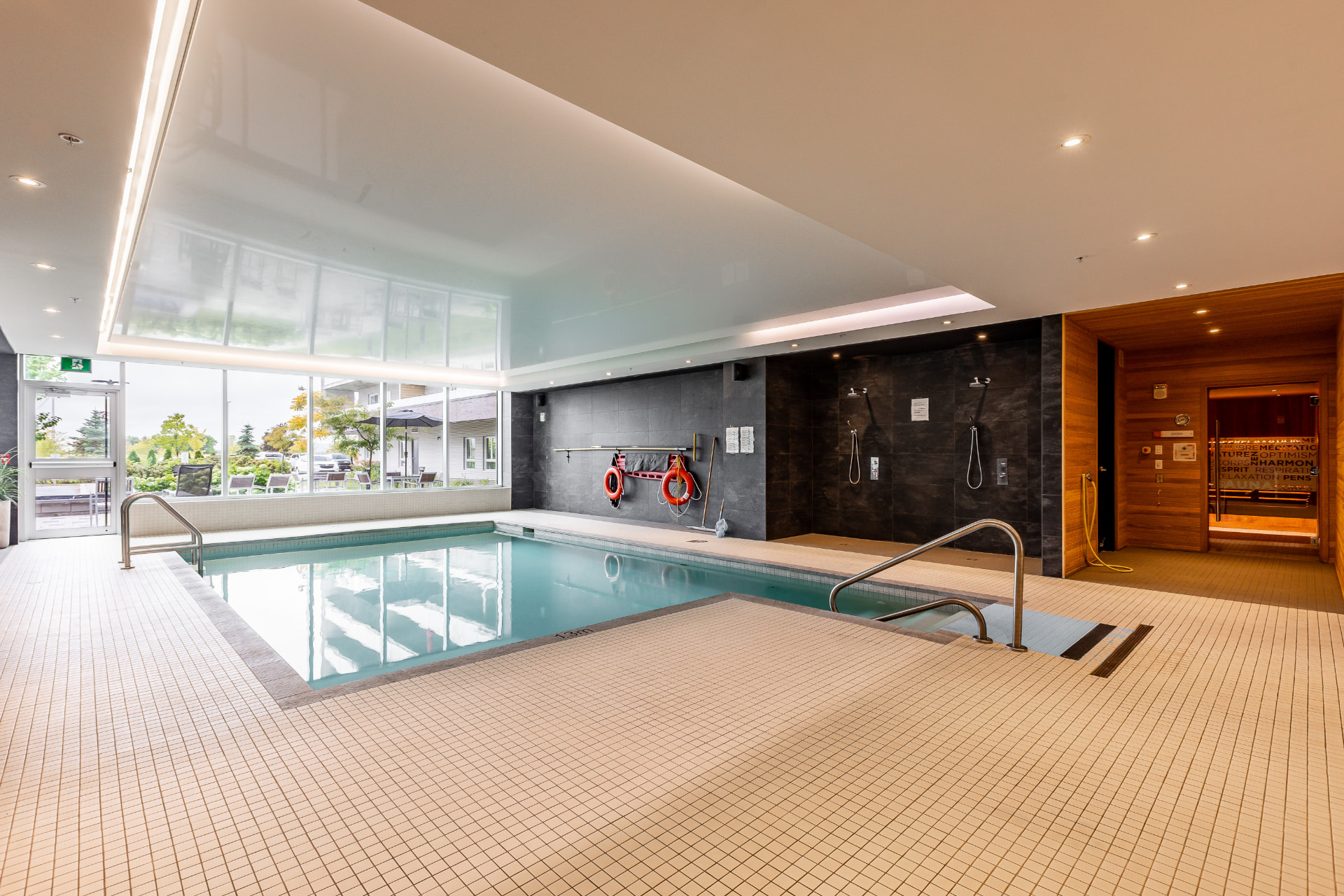 Piscine intérieure avec échelles chromées, tuiles claires et grandes fenêtres
