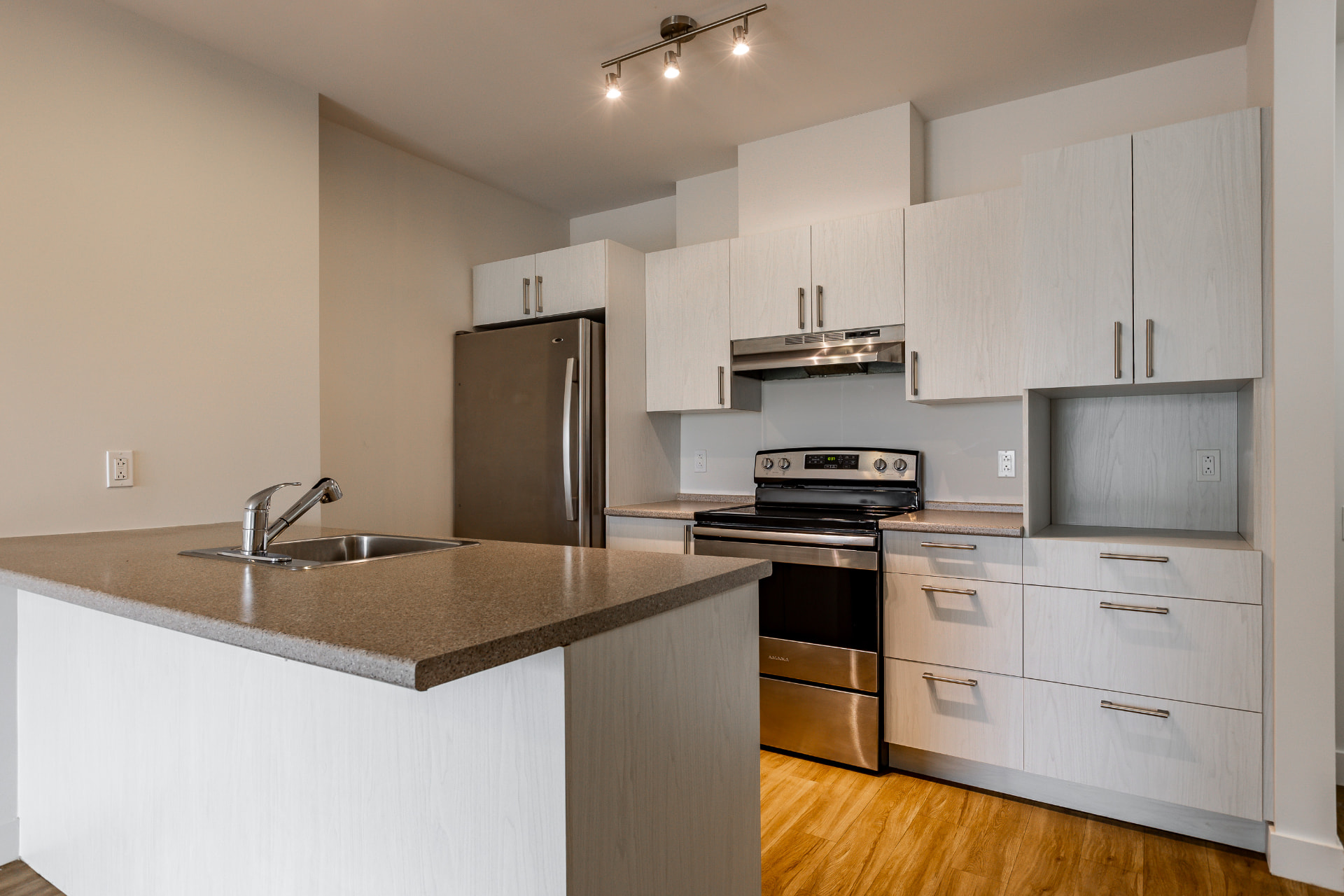 Cuisine d'appartement avec îlot, évier, armoires de bois clair et appareils inox