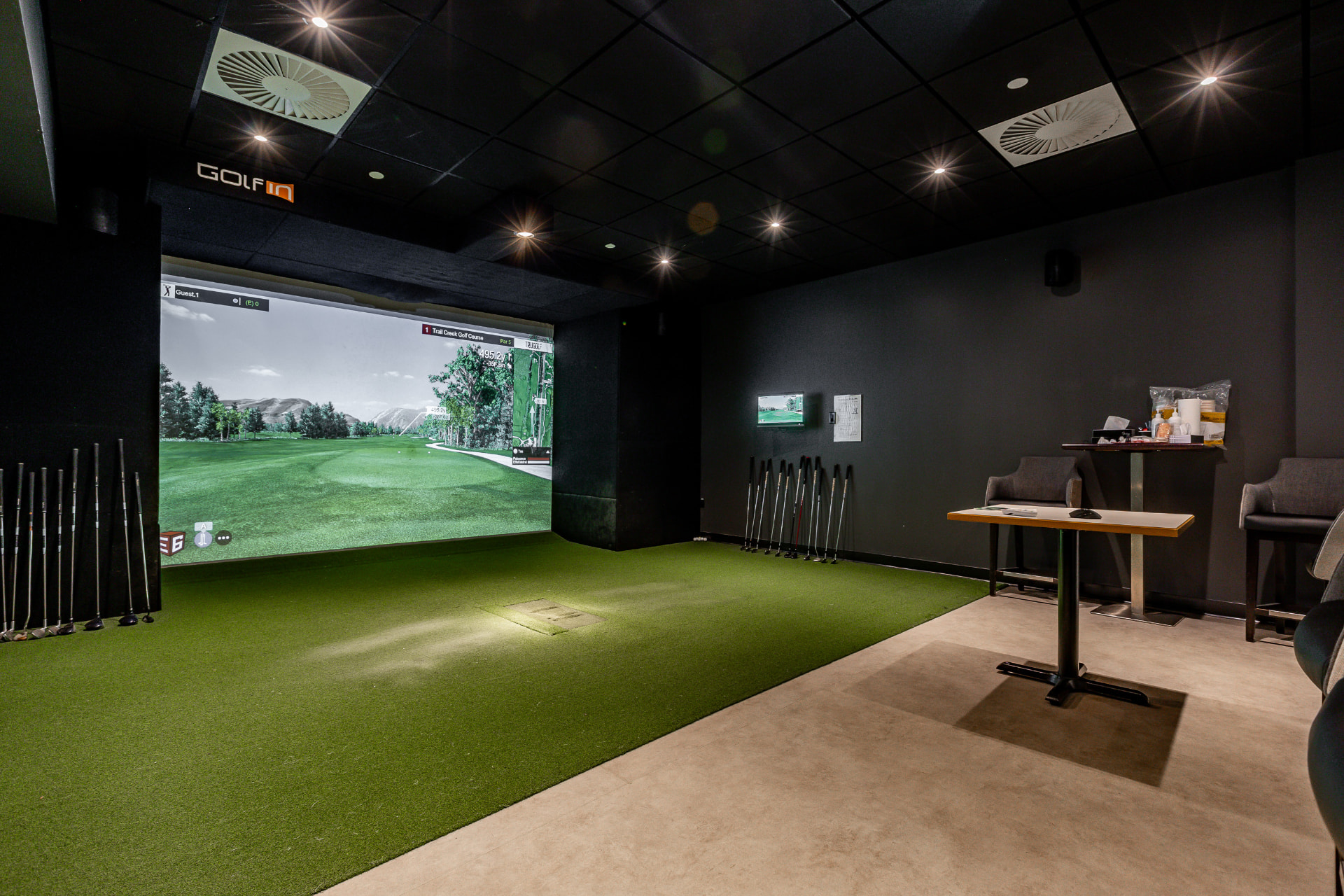 Salle de golf virtuel avec écran de projection, gazon synthétique et clubs
