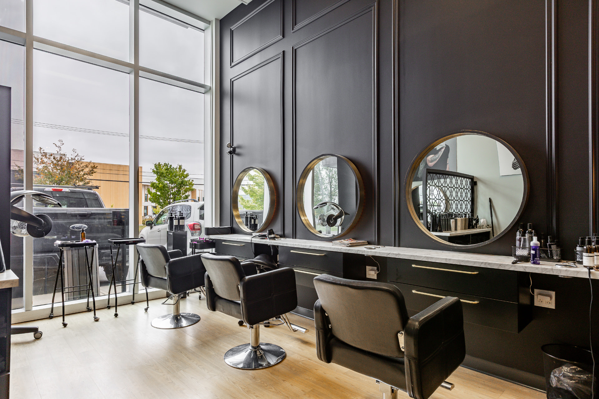 Salon de coiffure aux murs noirs, miroirs ronds et comptoir de marbre